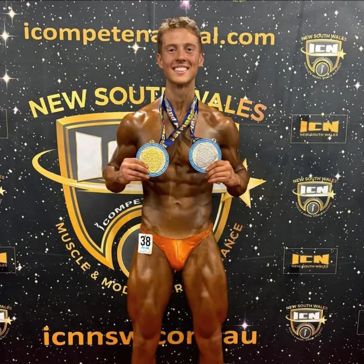 Corey-Jay Eyndhoven on stage at a natural bodybuilding show, holding two medals